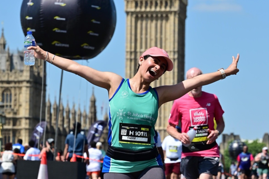 A woman runs towards the camera wearing a pink baseball cap. Big Ben is in teh background behind her.