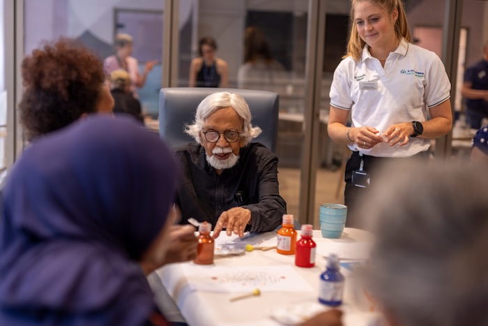 An art therapy session taking place in the Wellbeing Centre. A patient is painting with red and orange coloured paints.